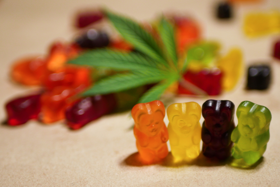 Gummy bears sit in a row with a cannabis leaf behind them