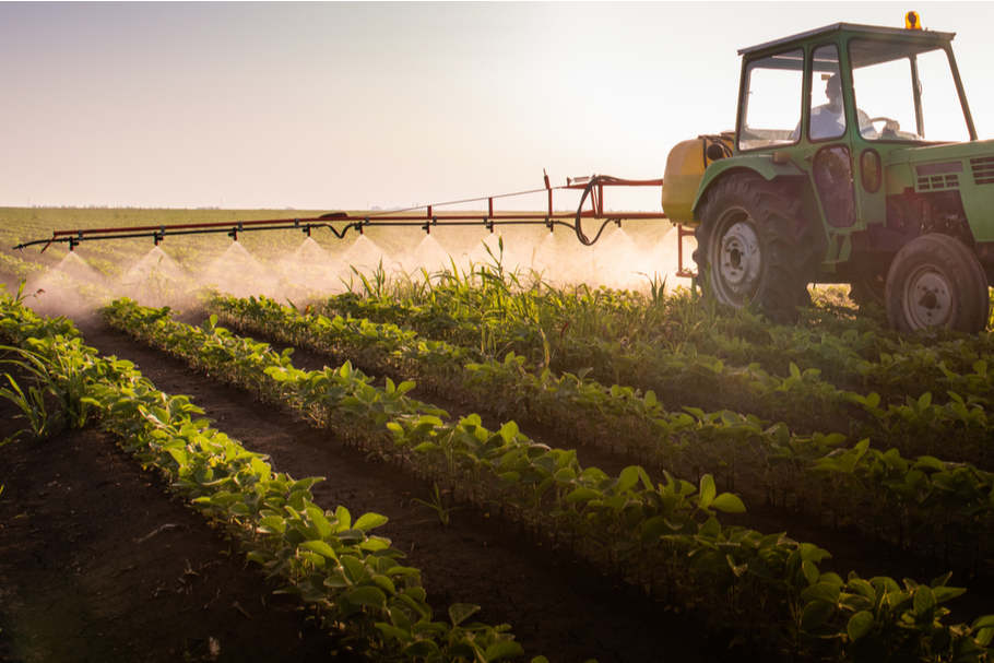 a tractor sprays pesticides over a growing crop