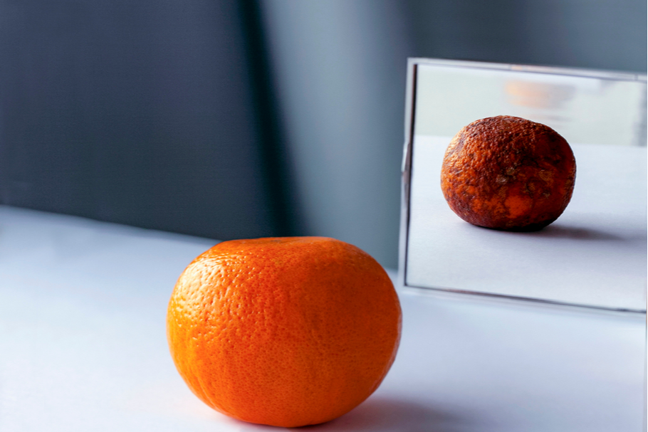 A healthy orange is reflected in a mirror, and its reflection is covered in mold