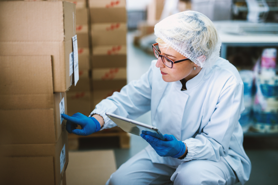 A food factory worker carefully examines the label on a box while holding a tablet.