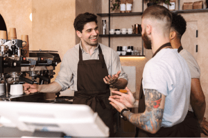 a young barista makes a coffee while talking with his coworkers
